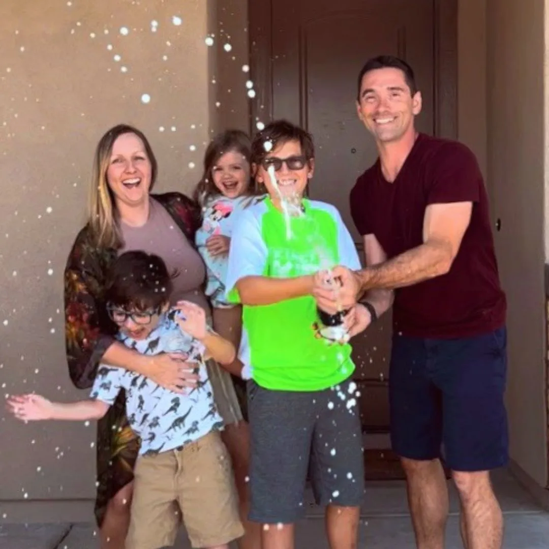 family popping champagne in front of new home