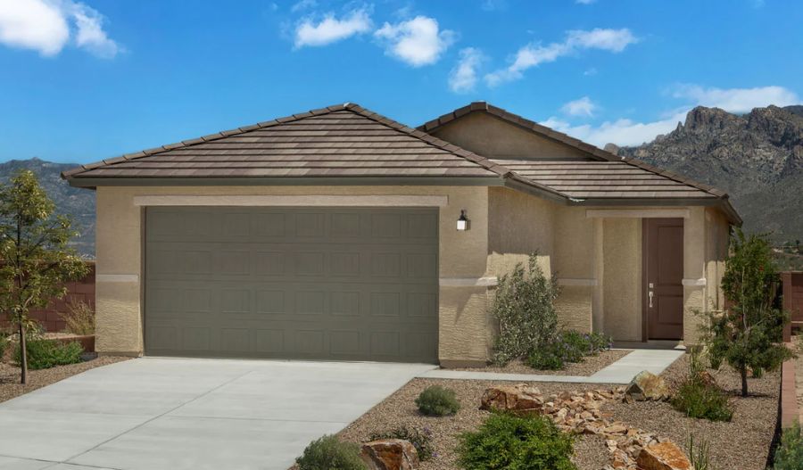 A single-story beige house with a gray double garage, brown tiled roof, and a front yard with desert landscaping. Mountains and a partly cloudy blue sky are visible in the background.