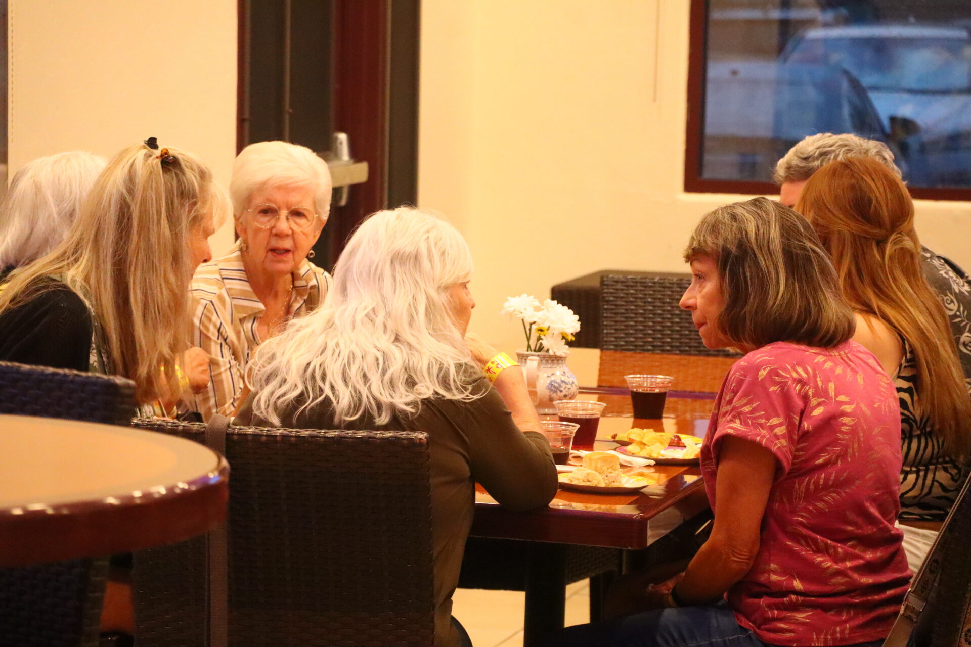 Five women sit around a table at a restaurant, talking and eating together.