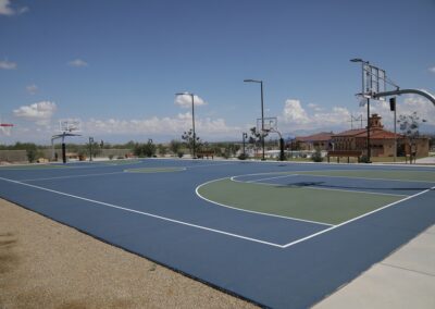 Outdoor basketball court with blue and green pavement, hoop systems, and benches under a clear sky.