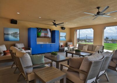 Outdoor covered patio lounge featuring multiple seating areas with wood-framed chairs and sofas facing a television cabinet.