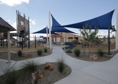 A modern playground with climbing structures and rock features shaded by large blue triangular sails.