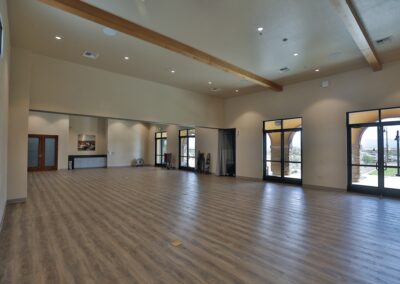 An empty multipurpose room with light wood floors, beige walls, floor-to-ceiling mirrors on one side, and several glass-paned doors leading to an outdoor patio.