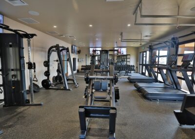 A well-lit fitness center featuring a leg press machine in the center, flanked by treadmills on the right and a weight station on the left.