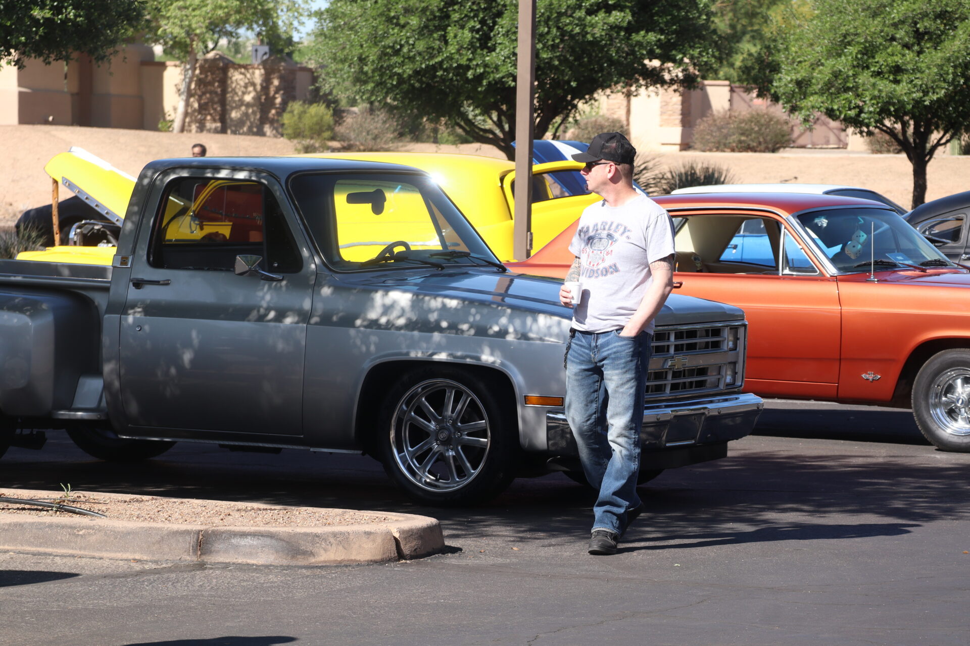 A man in a graphic t-shirt and jeans stands next to a silver vintage pickup truck at a car show.